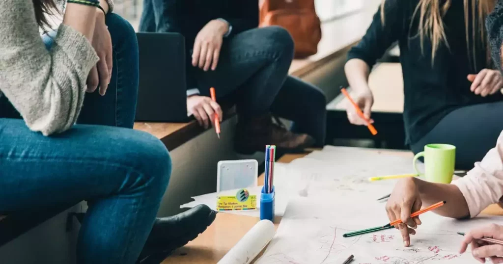 Pemimpin dan tim berdiskusi santai di ruang kerja modern, penuh senyum dan keterbukaan.
